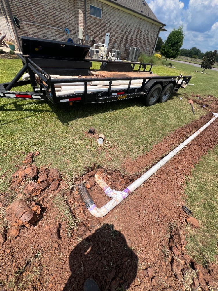 New water and sewer drain line installation with PVC pipe and utility trailer on a residential job site.
